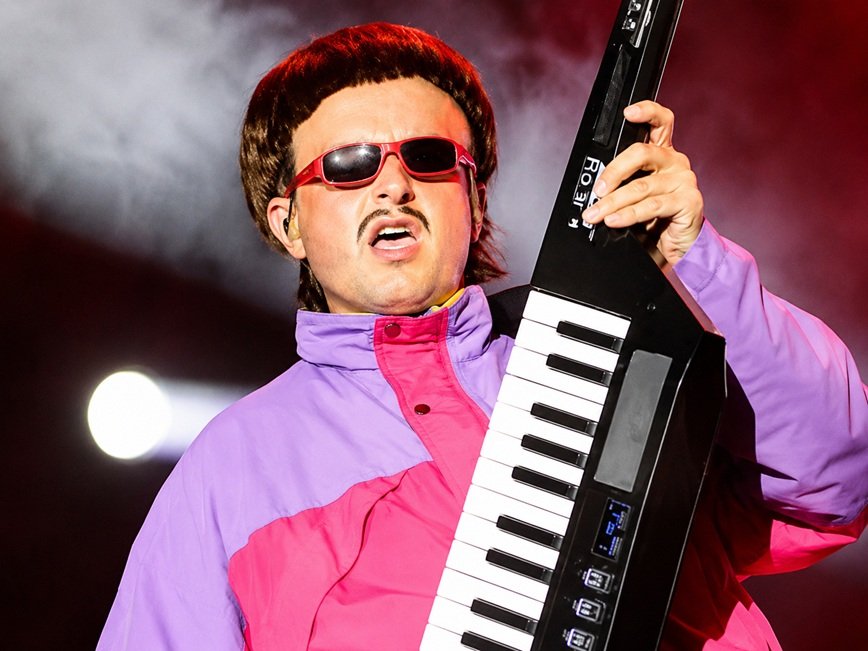 Oliver Tree Helicopter Accident tribute image showing the musician performing on stage with memorial-themed background